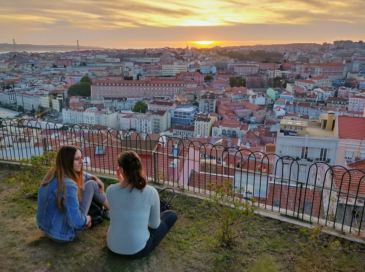 Two young women sitting on a Lisbon viewpoint at sunset