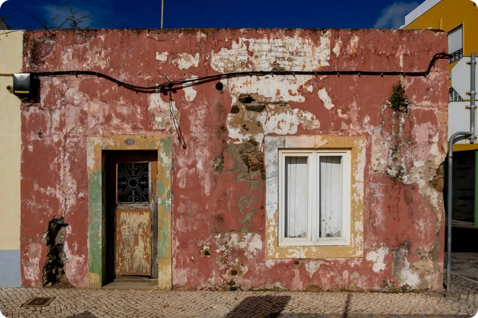 Une maison rouge patinée, au crépi écaillé et à la vieille porte en bois, dans une rue pavée au Portugal