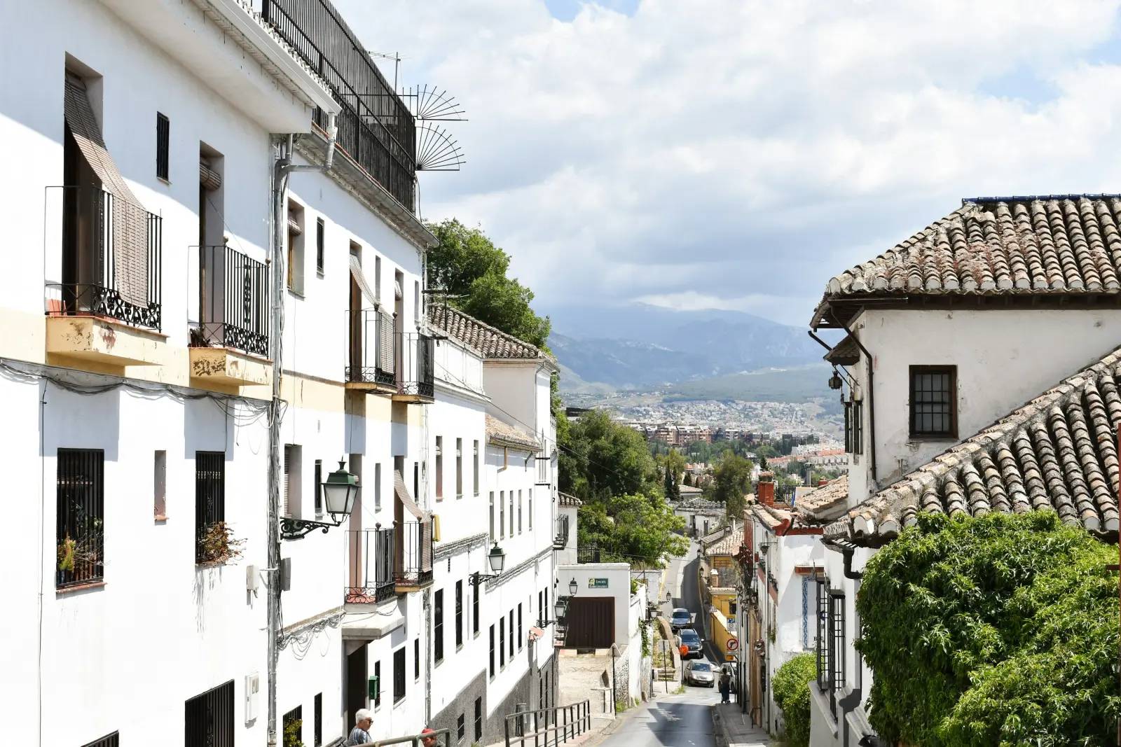 Whitewashed street running downhill to parked cars, with mountains behind, in Granada, Spain